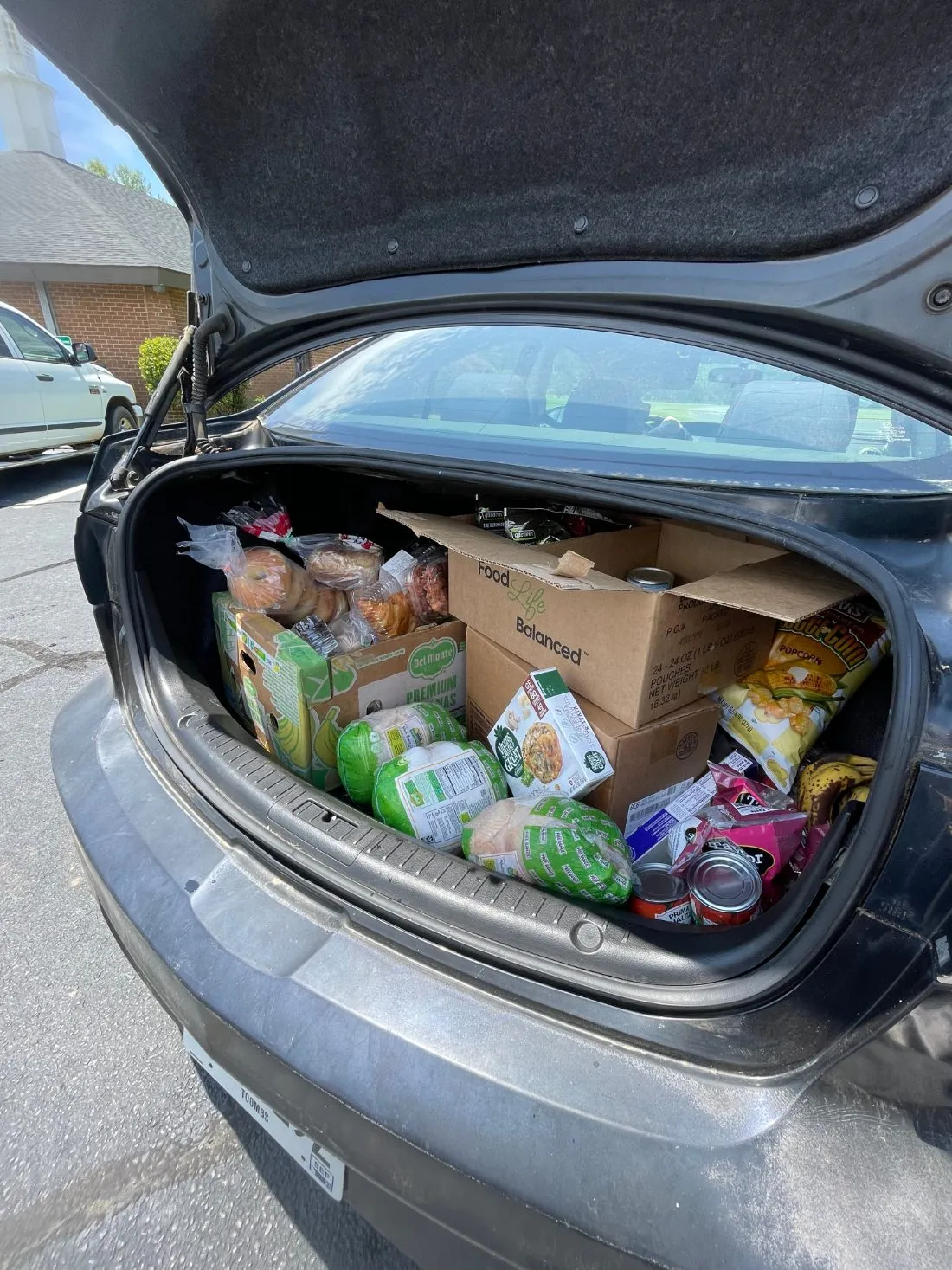 A car trunk filled with boxes of fresh groceries, bread, and produce